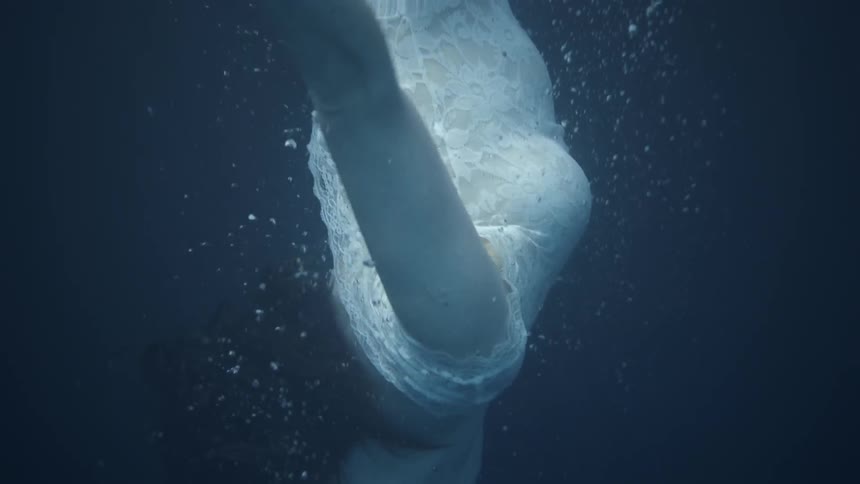 A woman in a white dress swims underwater