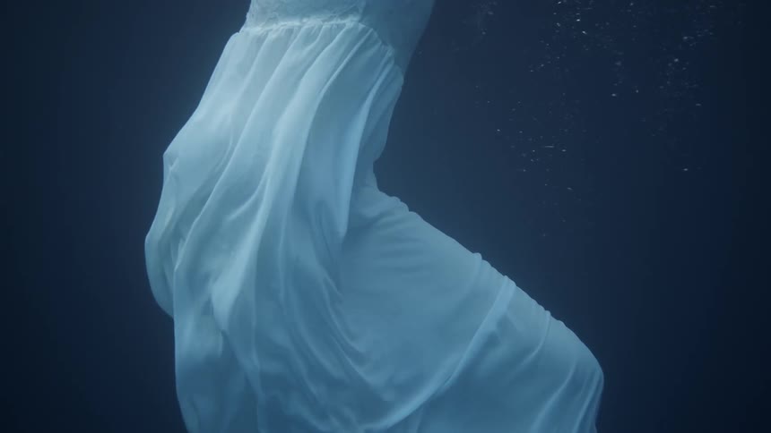 Woman wearing a dress floats under the water as she moves her arms