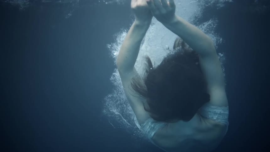 Woman wearing a white dress splashes down into a pool of water