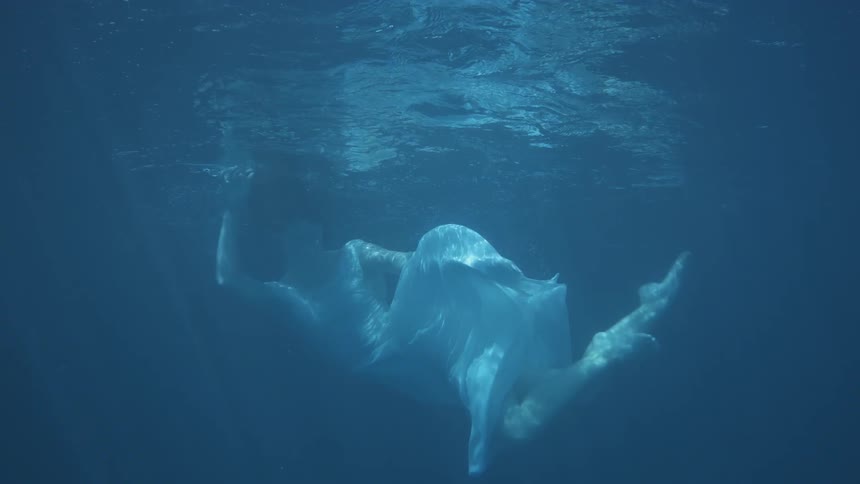Woman wearing a white dress spins around under water