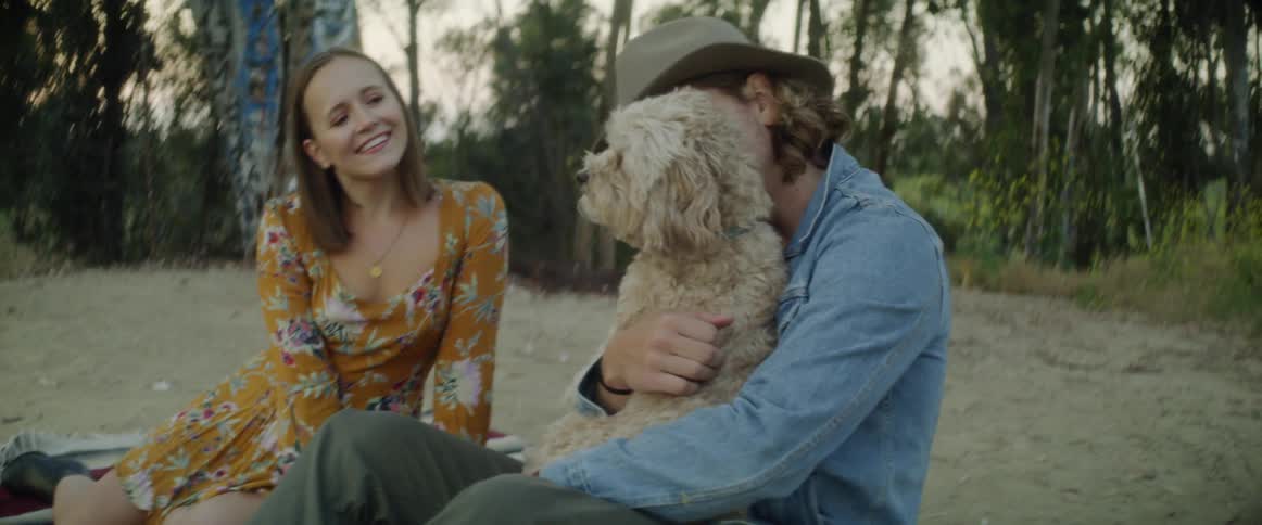 A couple are sitting on the ground in a natural setting and petting their dog