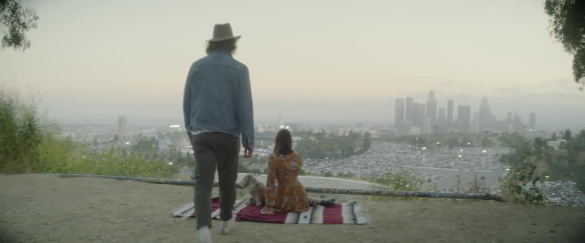 Woman and dog sit on a blanket as a man joins them