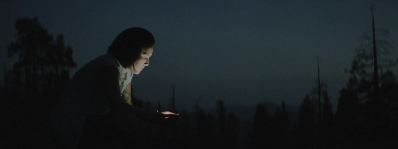 A woman uses her phone in a dark forest