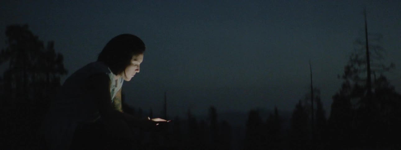 A person sits in the dark looking at a phone