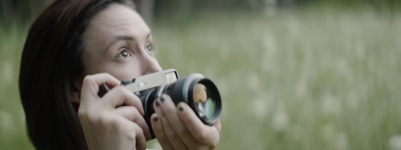 A photographer is pulling her camera away from here eyes outside in daylight