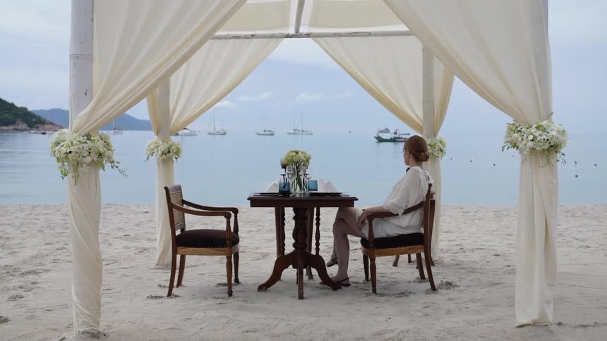 A woman sits under a canopy on the beach