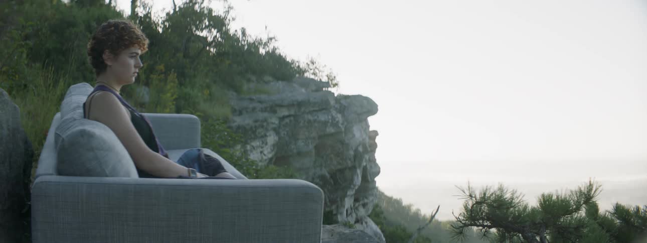 A woman sits on a sofa in mountains