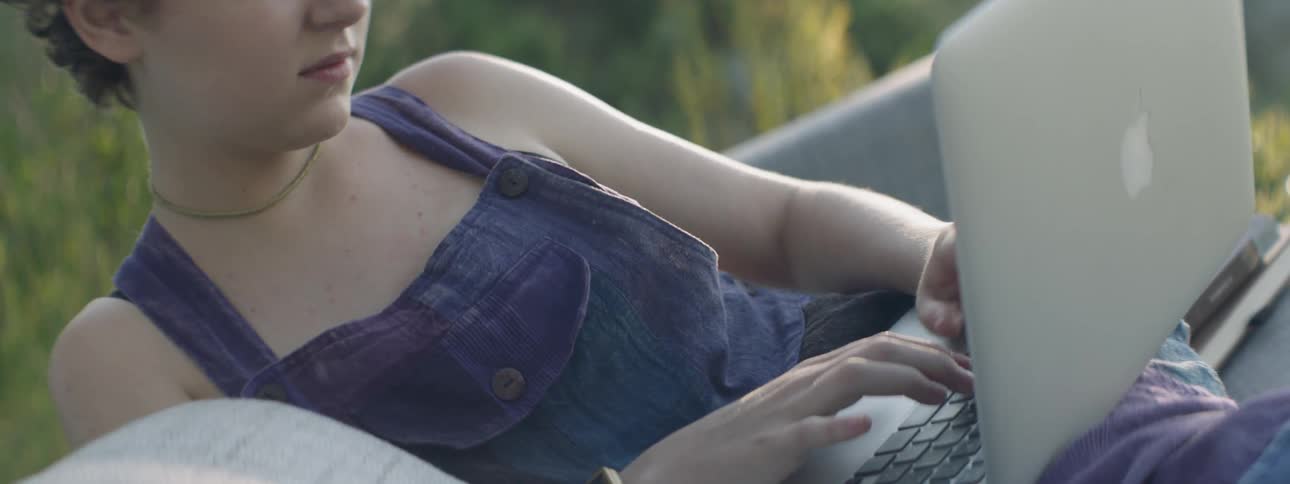 A woman types on a laptop on a sofa outside