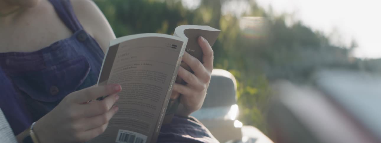 A woman reads a book on sofa outside