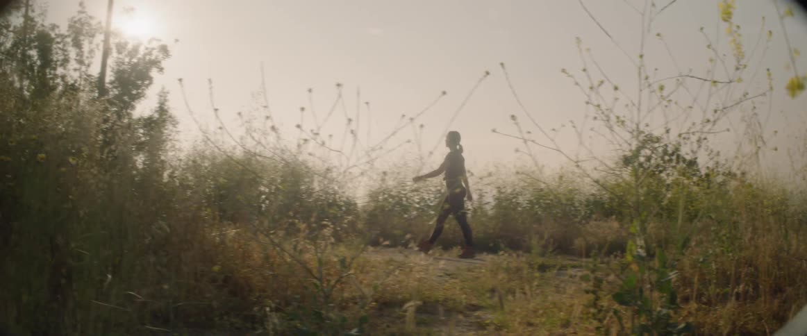 A woman walks in a rural field with tall weeds