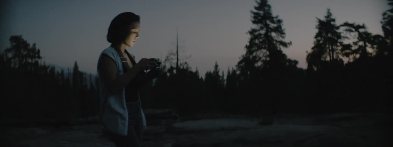 A woman uses a camera outside at dusk