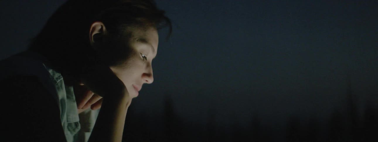 Man sits outside at night looking down at something lit up