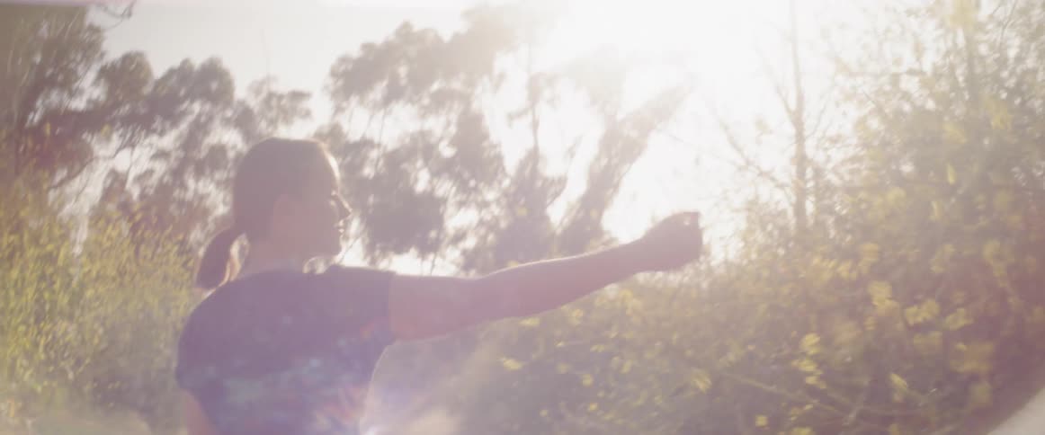 A woman touches plants in a sunny meadow