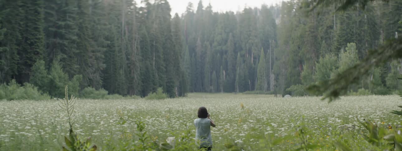 A woman walks through a field of weeds and grass