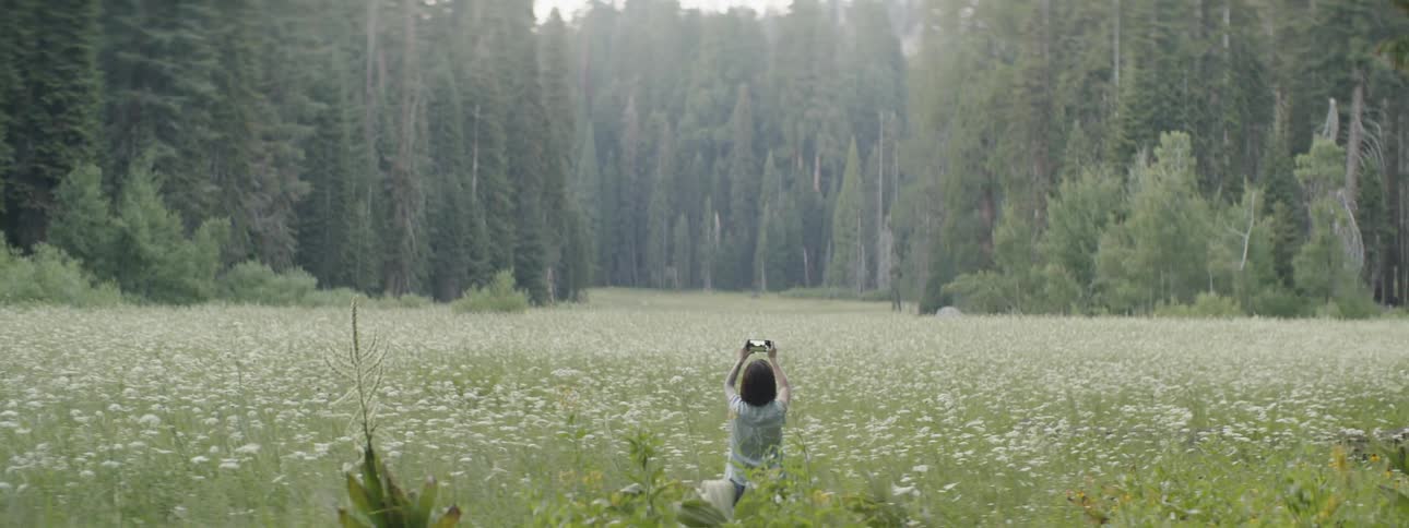 Woman sits in a field and takes a photo