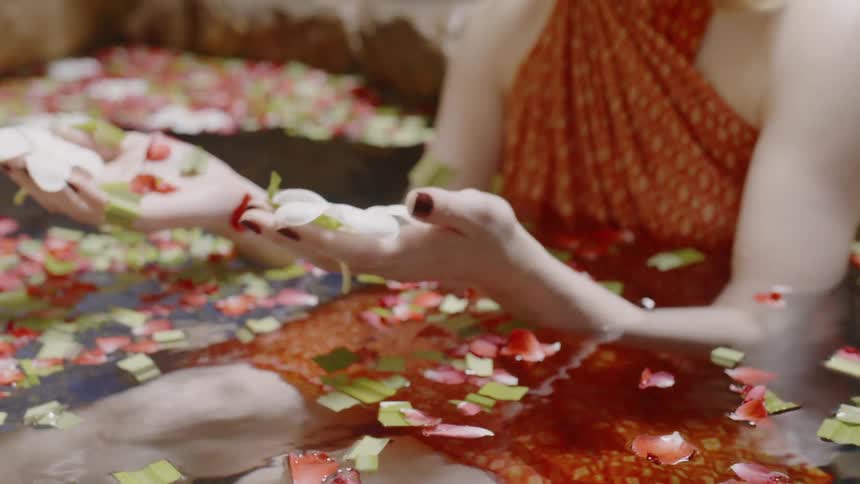 Woman sitting in water lifts flower petals