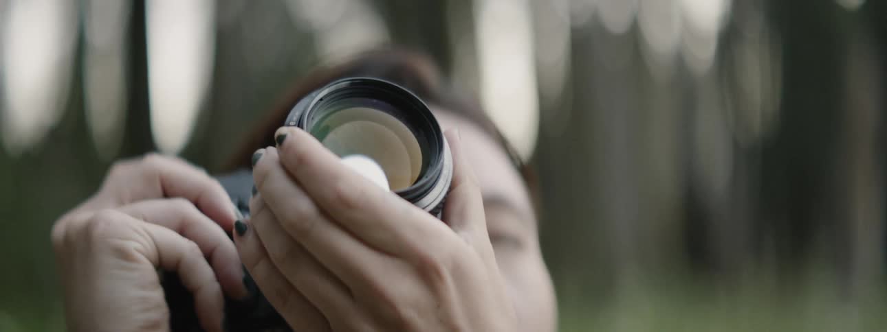 A photographer is raising her camera to take photos outside in a natural setting in daylight