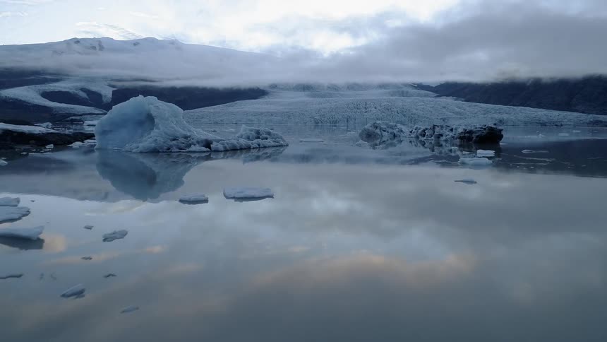 Clouds are hanging over a glacier and icebergs at dawn