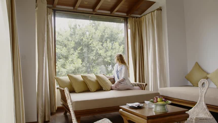 A woman is sitting on a couch and enjoying a view from a window in daylight