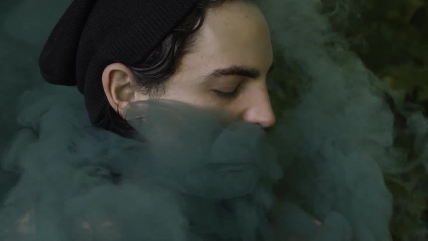 Colored smoke floats around a man who has his eyes closed