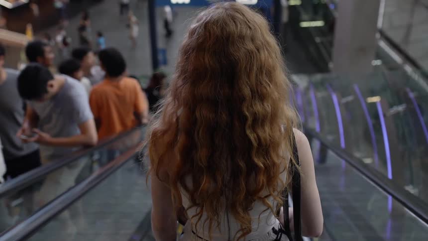 Woman rides an escalator down and several people ride an escalator up
