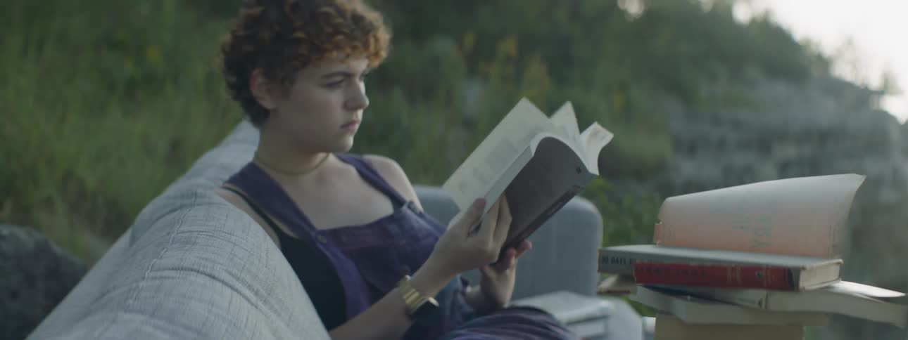 A woman reads a book on a sofa outside