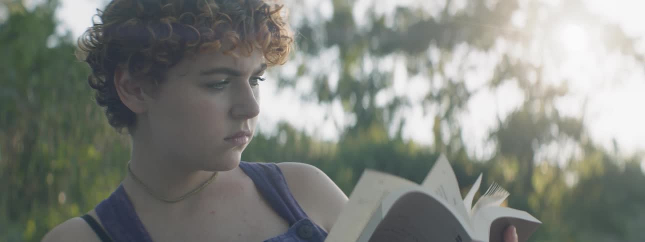 Young woman flips through a book as she sits near the trees