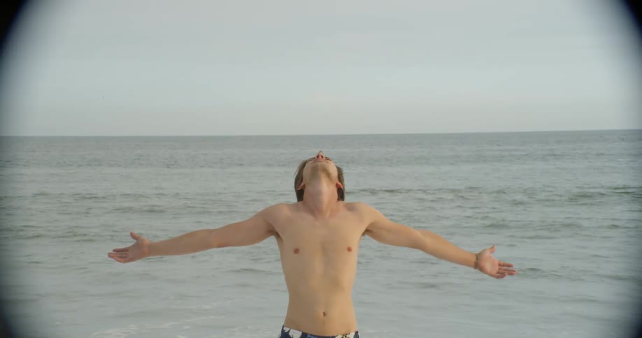Man wearing swim trunks stands with his back to the water