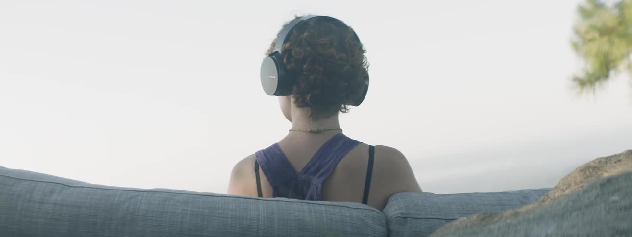 A woman sits outside with headphones on