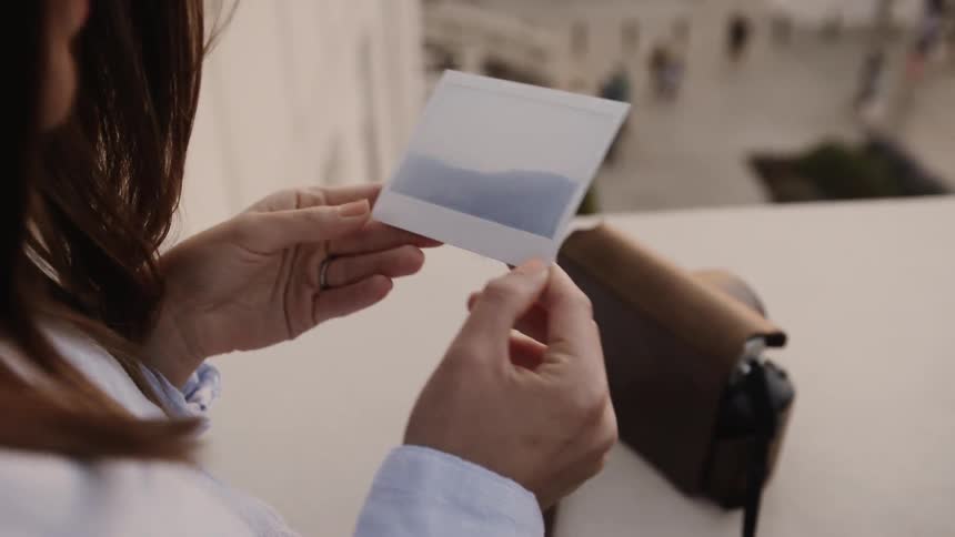 A woman holds a photograph on a balcony
