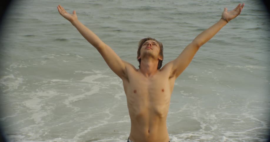 A man stands on a beach with his arms outstretched