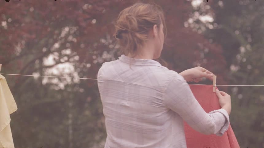 A woman is removing laundry from a line outside as smoke wafts past her