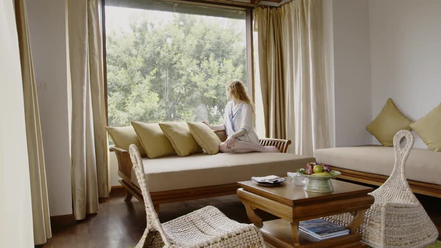 Woman is sitting on couch in home and looking out window