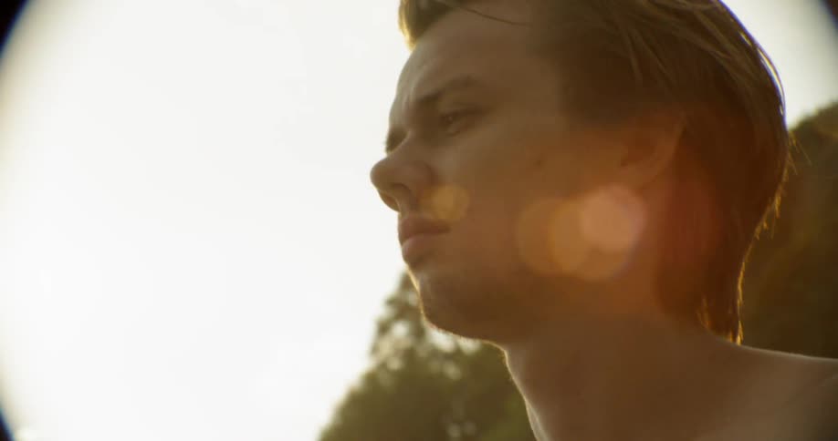 A shirtless man stands outside at sunset