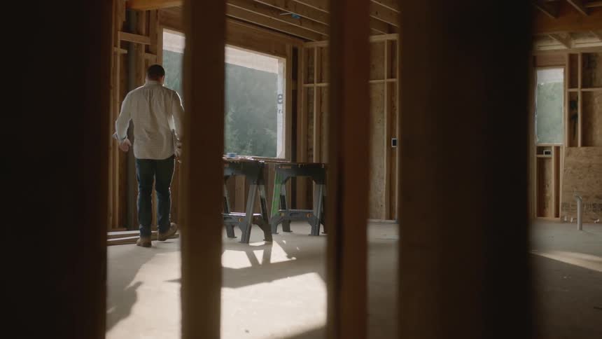 Man walks into an empty room with rolls of paper and puts them on a workbench