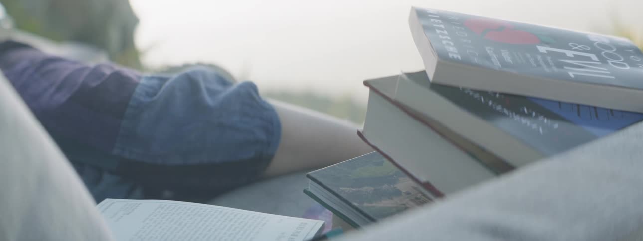 A person sits next to a pile of books outside