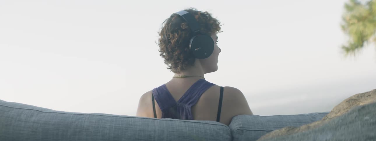 Woman wearing headphones sits on a couch outside