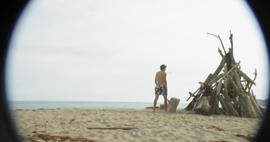 A man walks by a pile of wood on a sandy beach