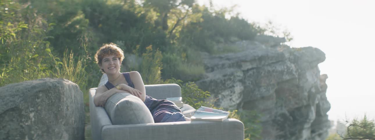 Woman smiles as she sits on a sofa outside