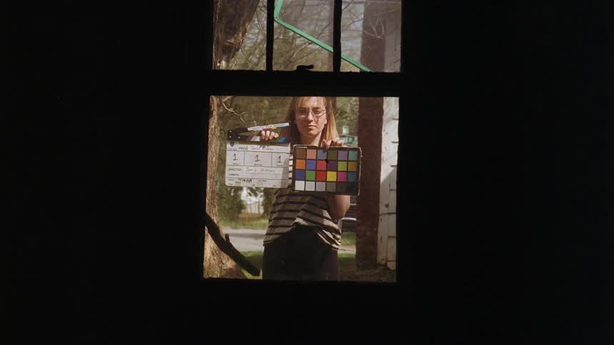 A woman holds filming equipment outside of a window