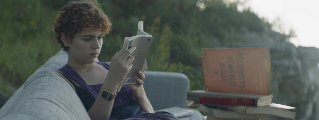 A woman reads a book on a sofa outside