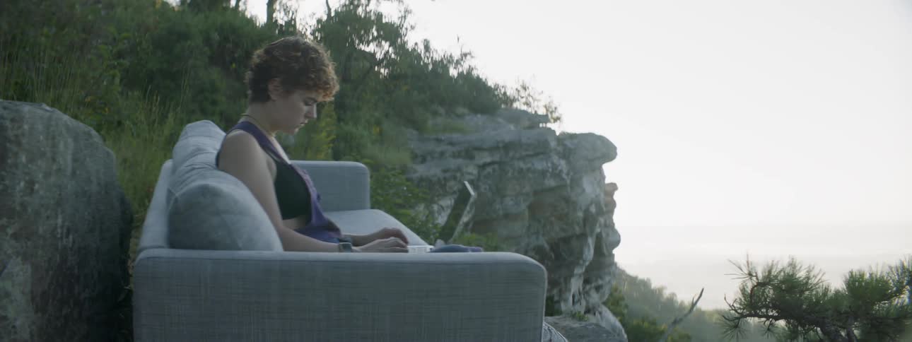 A woman types on her keyboard on the couch outside