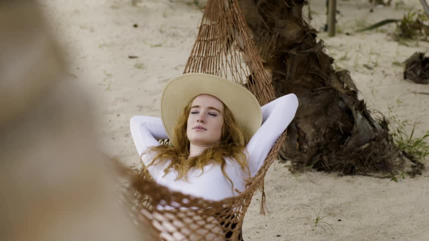 A woman relaxes in a hammock on a beach