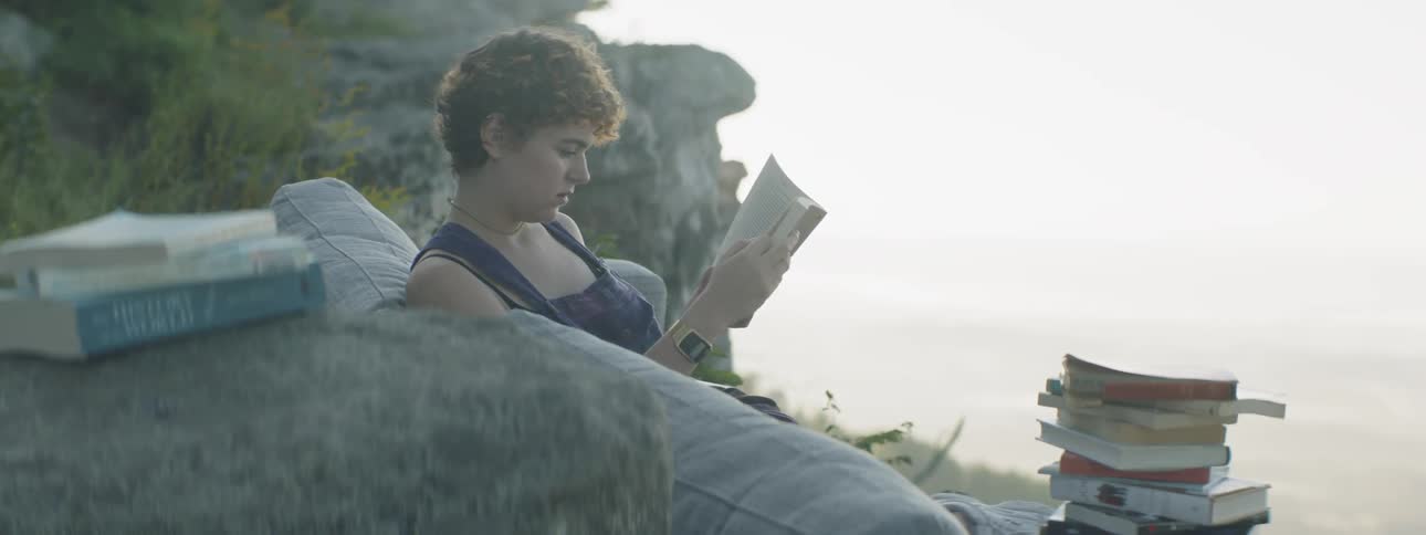 A woman reads a book on a sofa outside