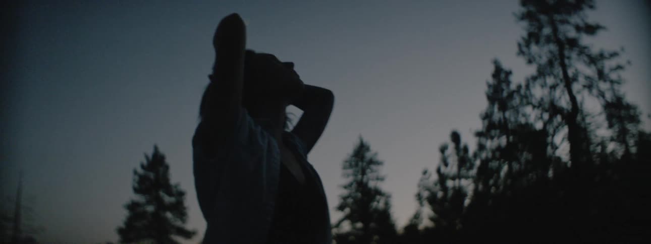 Woman stands outside near trees at sunset