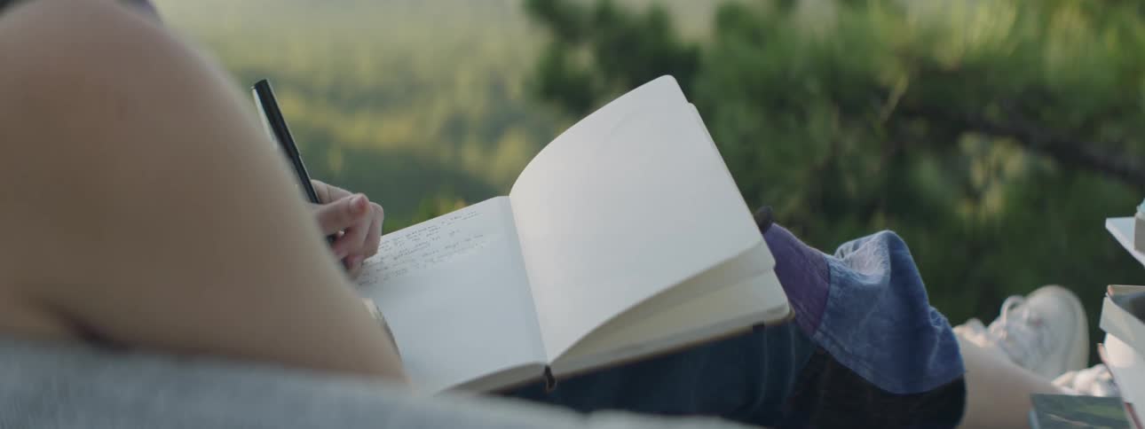 Woman writes with her left hand in a notebook as she sits outside