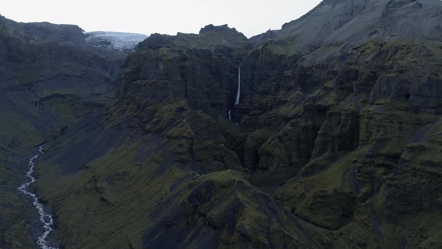 A waterfall is cascading over a cliff in a canyon in daylight