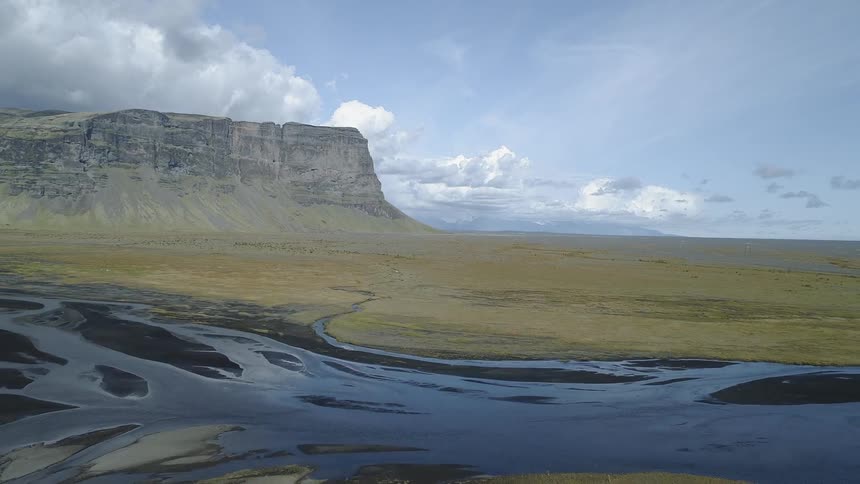 A stream runs through the green field to the mountain