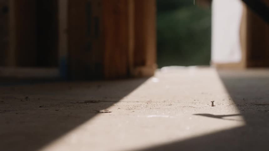 Hammer hits a nail on the floor in a room where the sun shines down