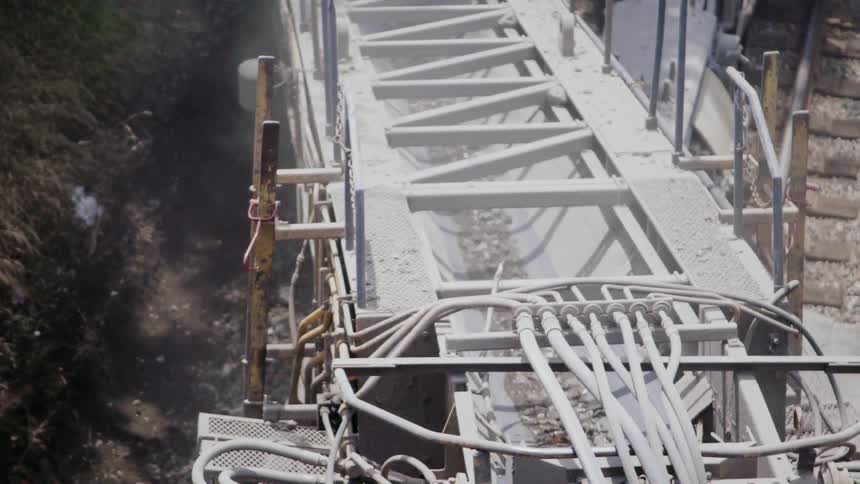 Rocks and dirt are moving through a chute over a ravine in daylight